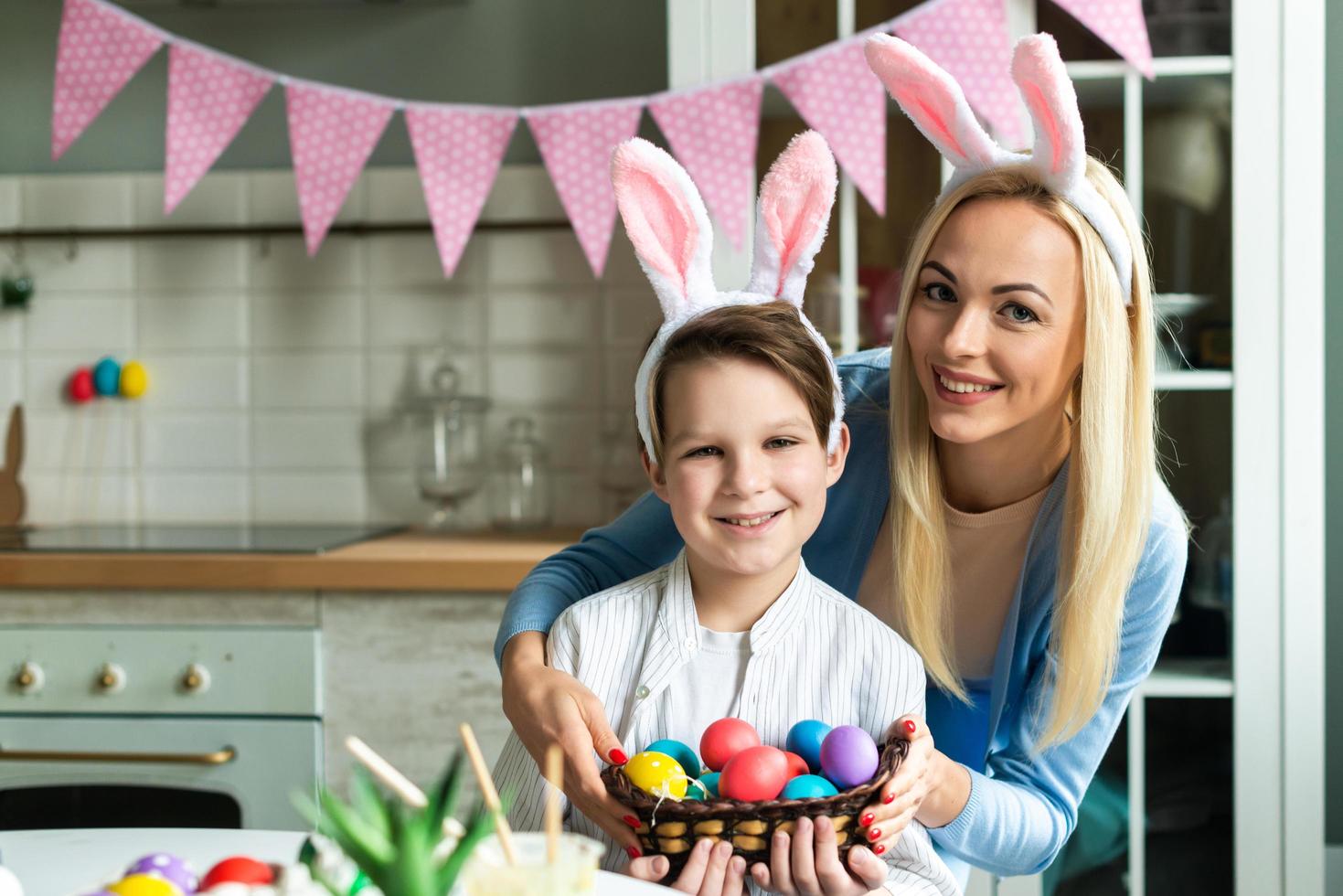 mamma sorridente con figlio in posa tenendo le uova di pasqua nelle orecchie di coniglio. foto