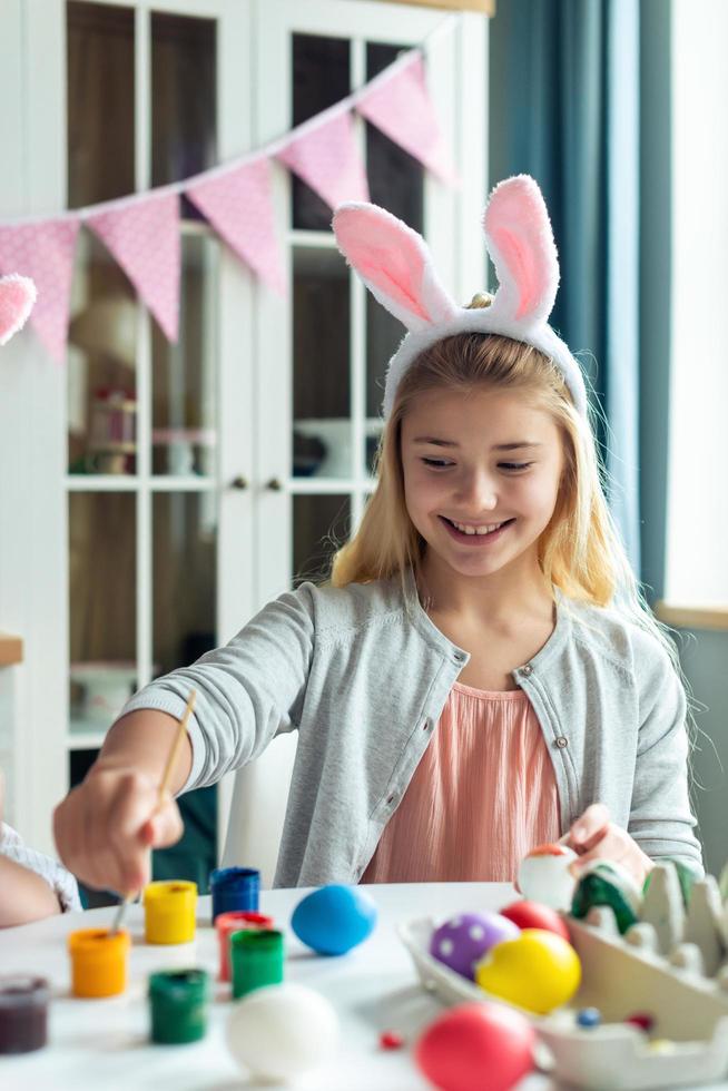 bella ragazza bionda con le orecchie da coniglio che colora le uova, buona pasqua foto