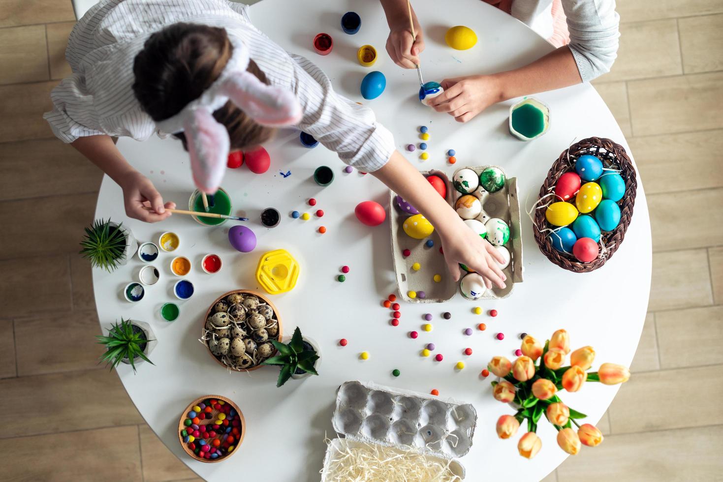 vista dall'alto, i bambini al tavolo dipingono le uova di Pasqua, le vernici, l'atmosfera di lavoro. foto