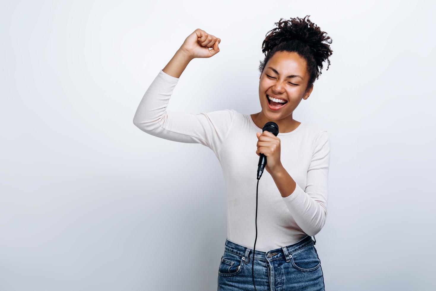 ragazza carina canta in un microfono, si diverte a cantare su uno sfondo bianco foto