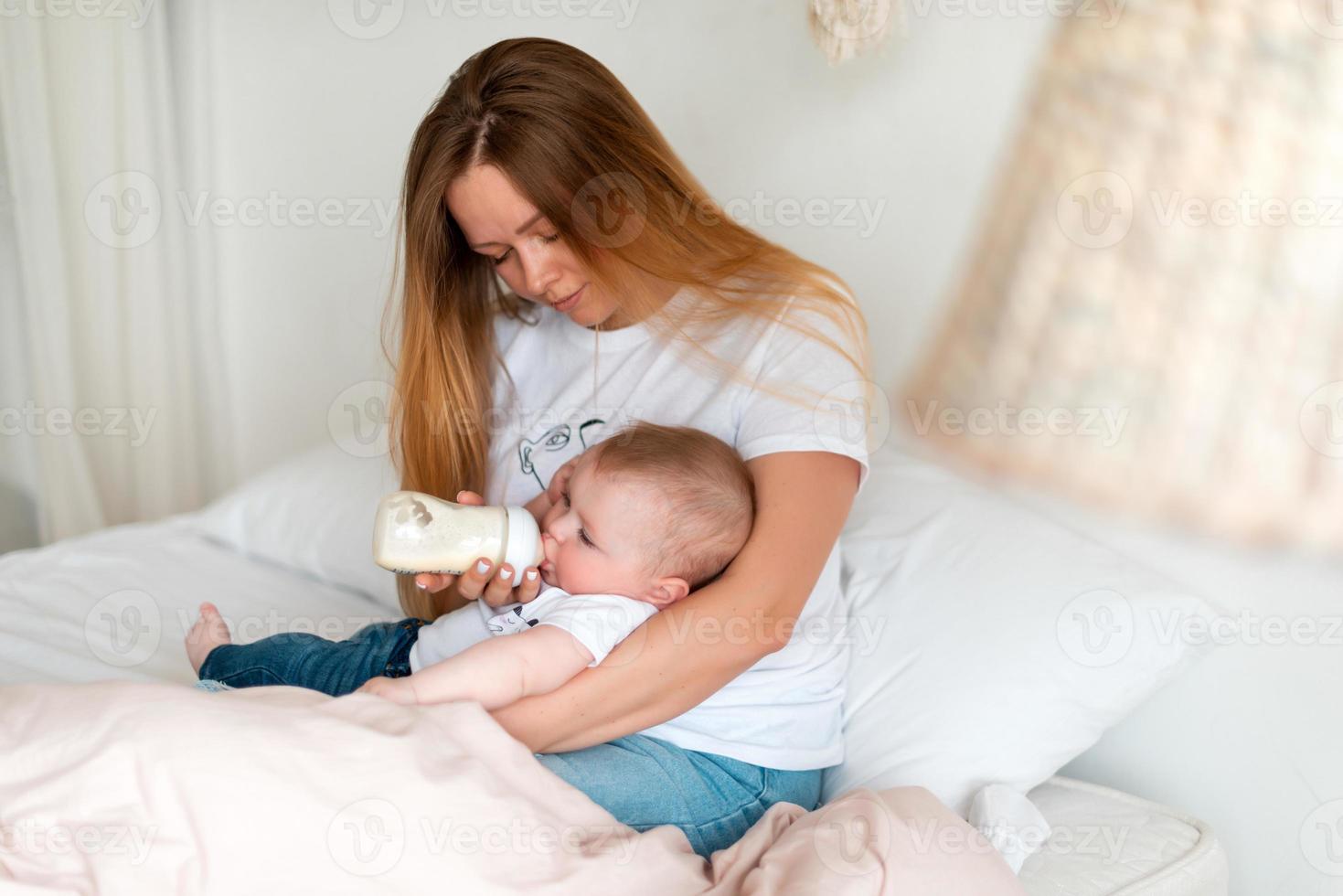una giovane e bella madre dà al suo bambino la pappa da una bottiglia foto