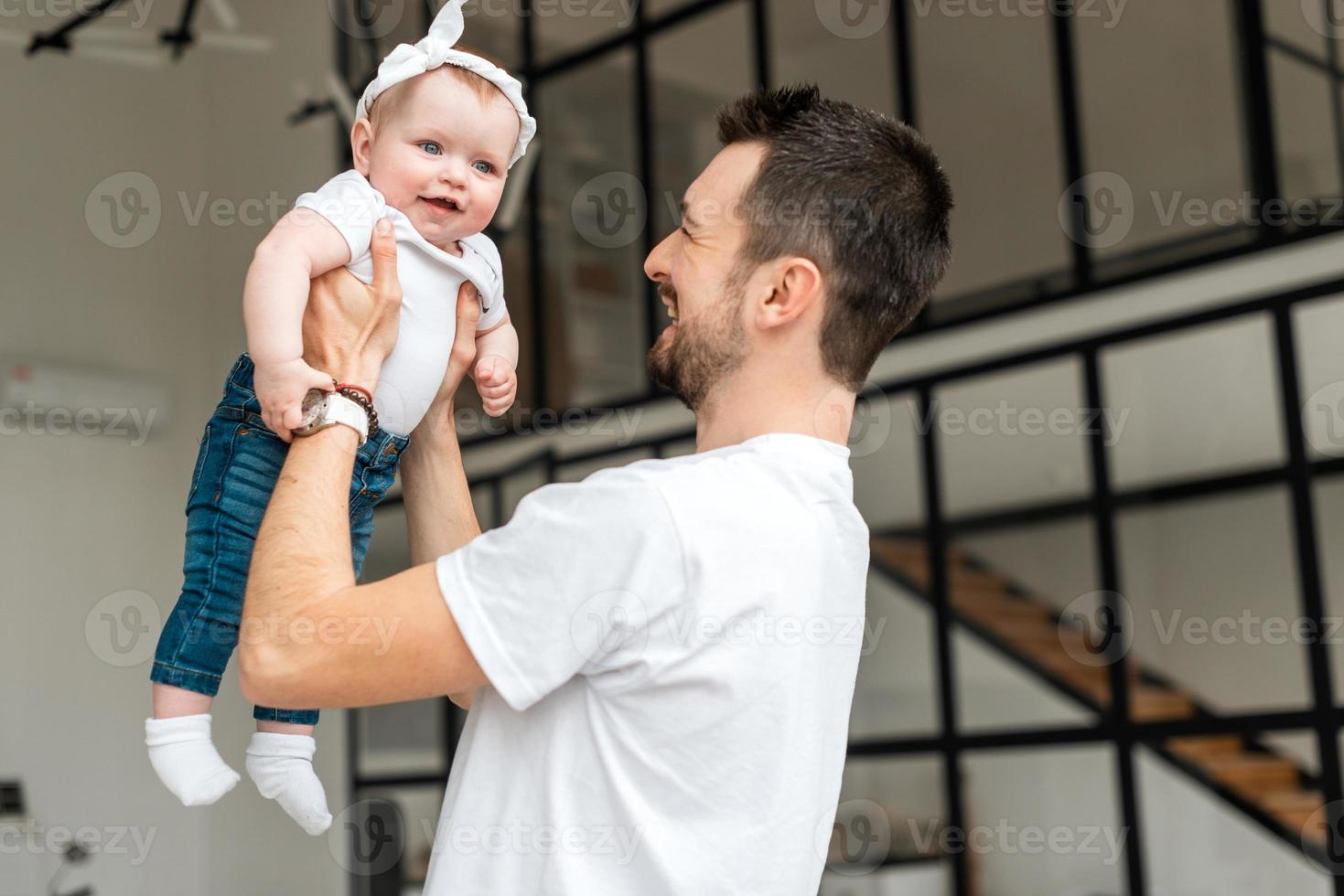 un giovane tiene in braccio la sua piccola figlia. bambina che sorride felice foto