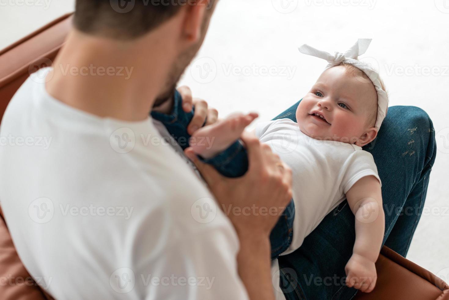 papà carino e amorevole bacia le piccole e tenere gambe della sua bellissima piccola figlia foto