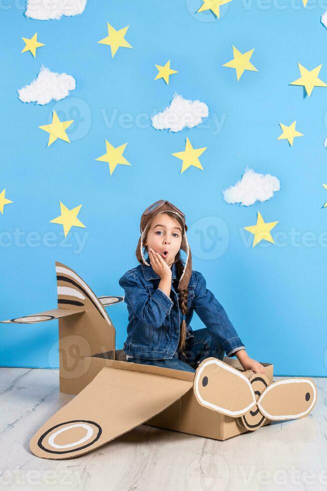 poco sognatore ragazza giocando con un' cartone aereo a il studio con blu cielo e bianca nuvole sfondo. foto