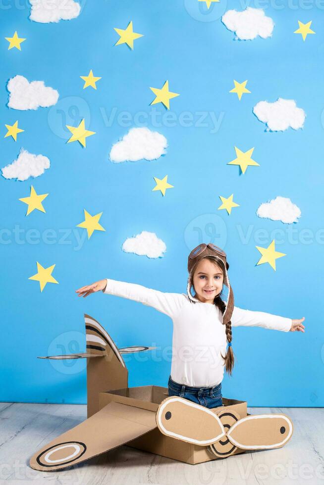 poco sognatore ragazza giocando con un' cartone aereo a il studio con blu cielo e bianca nuvole sfondo. foto