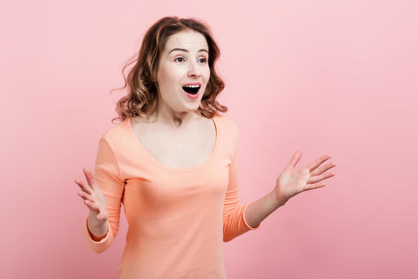 una bella ragazza piacevolmente sorpresa aprì le braccia contro un muro rosa foto