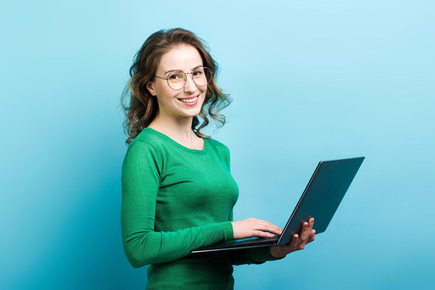 ritratto di una bella donna riccia sorridente con gli occhiali e che indossa un maglione verde con in mano un laptop foto
