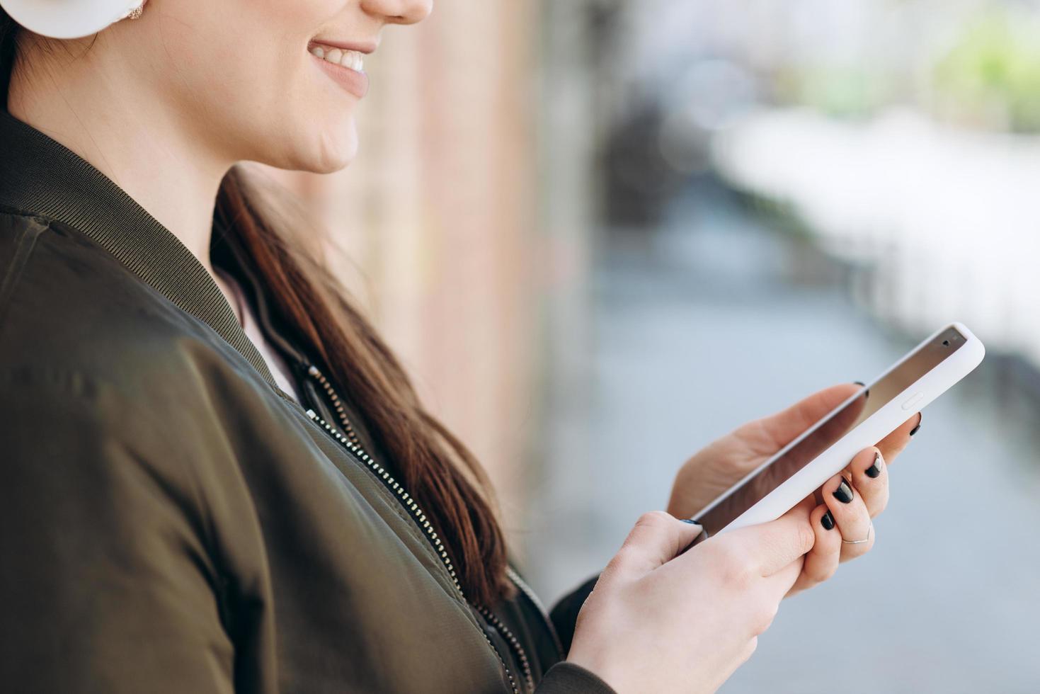 ragazza sorridente e gioiosa con le cuffie wireless si appoggia a un muro di mattoni, include la tua musica preferita foto