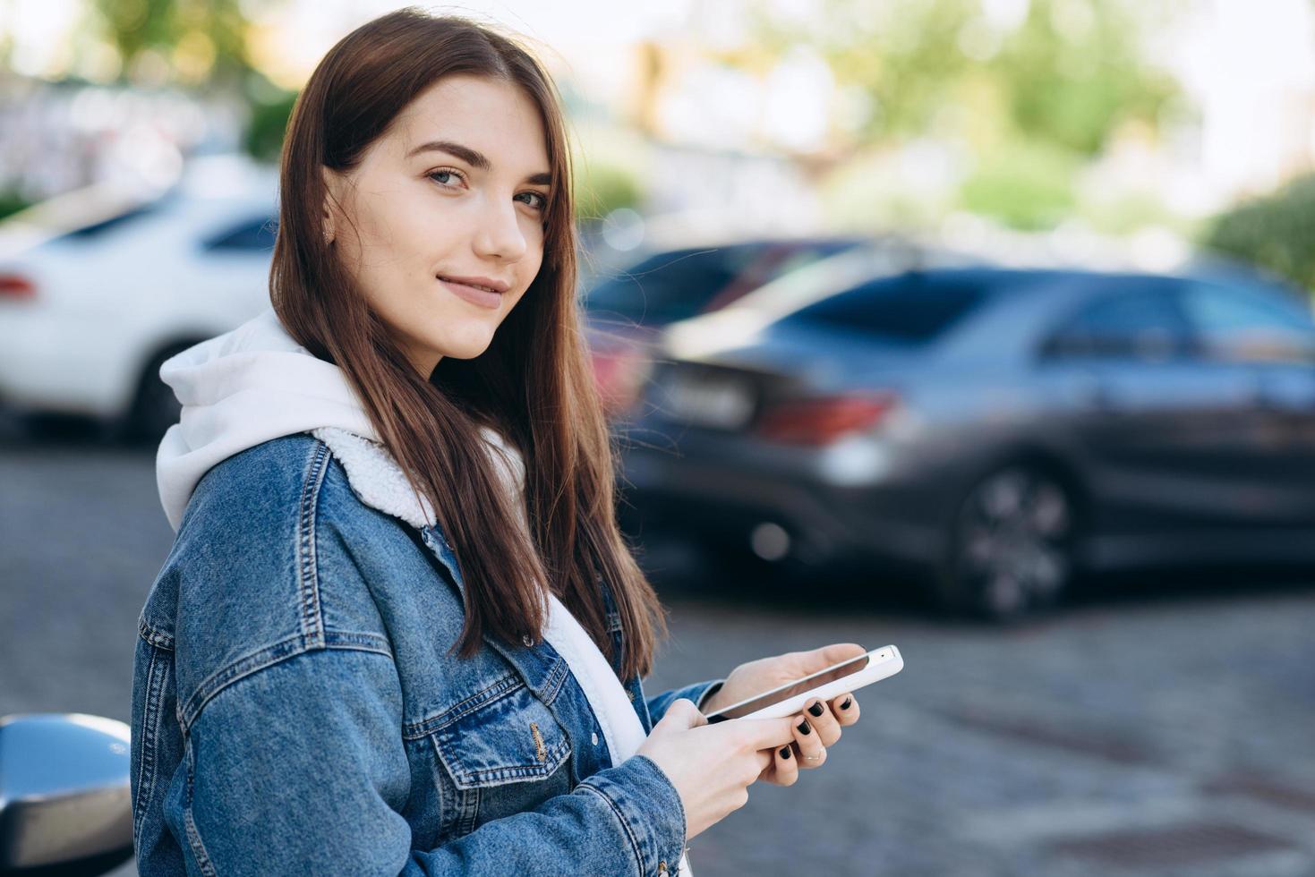 la ragazza giovane e attraente con i capelli neri sembra qualcosa in uno smartphone su una strada della città foto