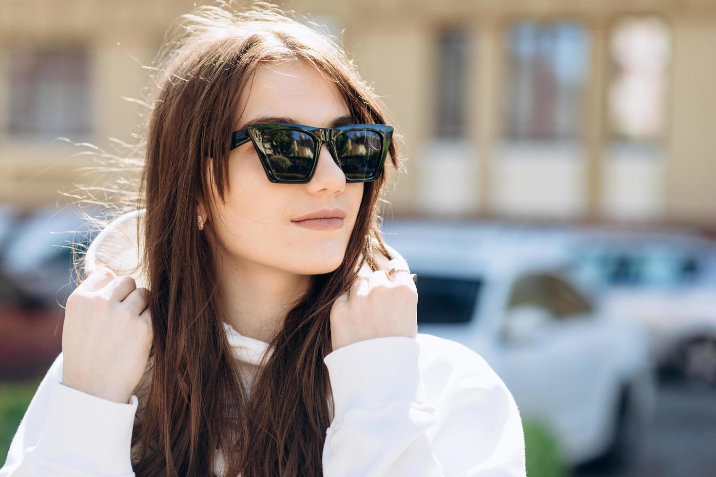 bruna carina e attraente in posa con occhiali da sole e un maglione bianco con cappuccio foto