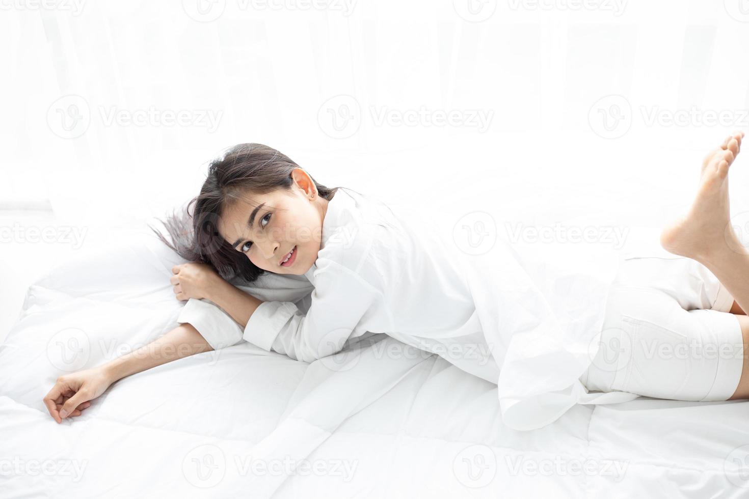 donna asiatica bella giovane donna sorridente seduta sul letto e stretching la mattina in camera da letto dopo essersi svegliata nel suo letto completamente riposata e aprire le tende al mattino per prendere aria fresca. foto
