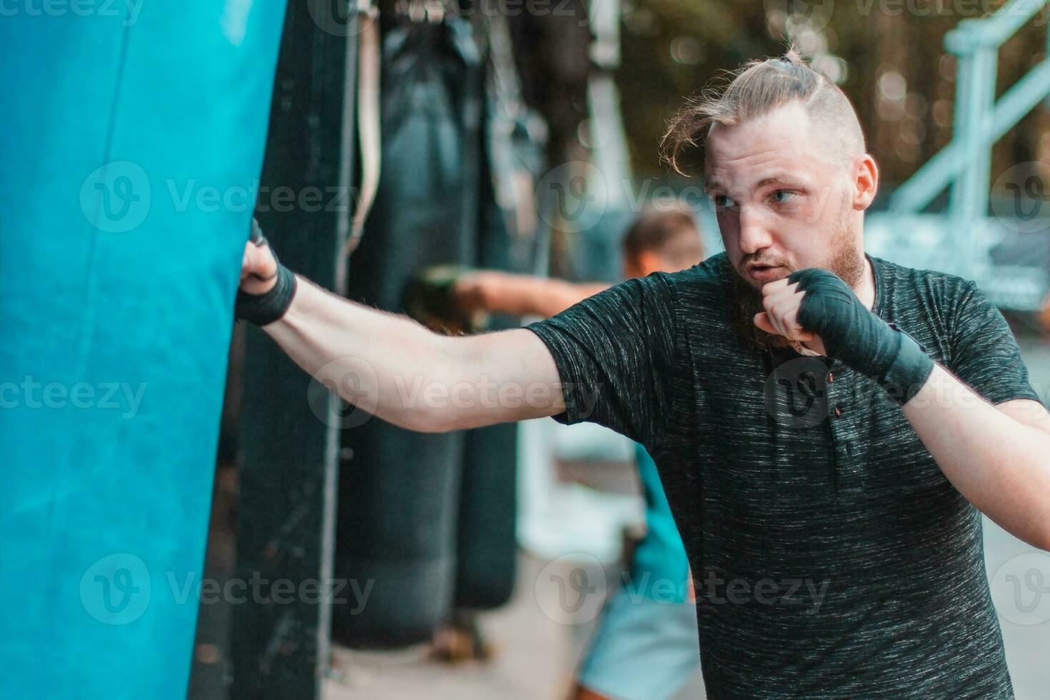 strada combattente nel nero Abiti e fasciature su il polso boxe nel punzonatura Borsa all'aperto. giovane uomo fare scatola formazione e praticante il suo pugni a il al di fuori Palestra foto