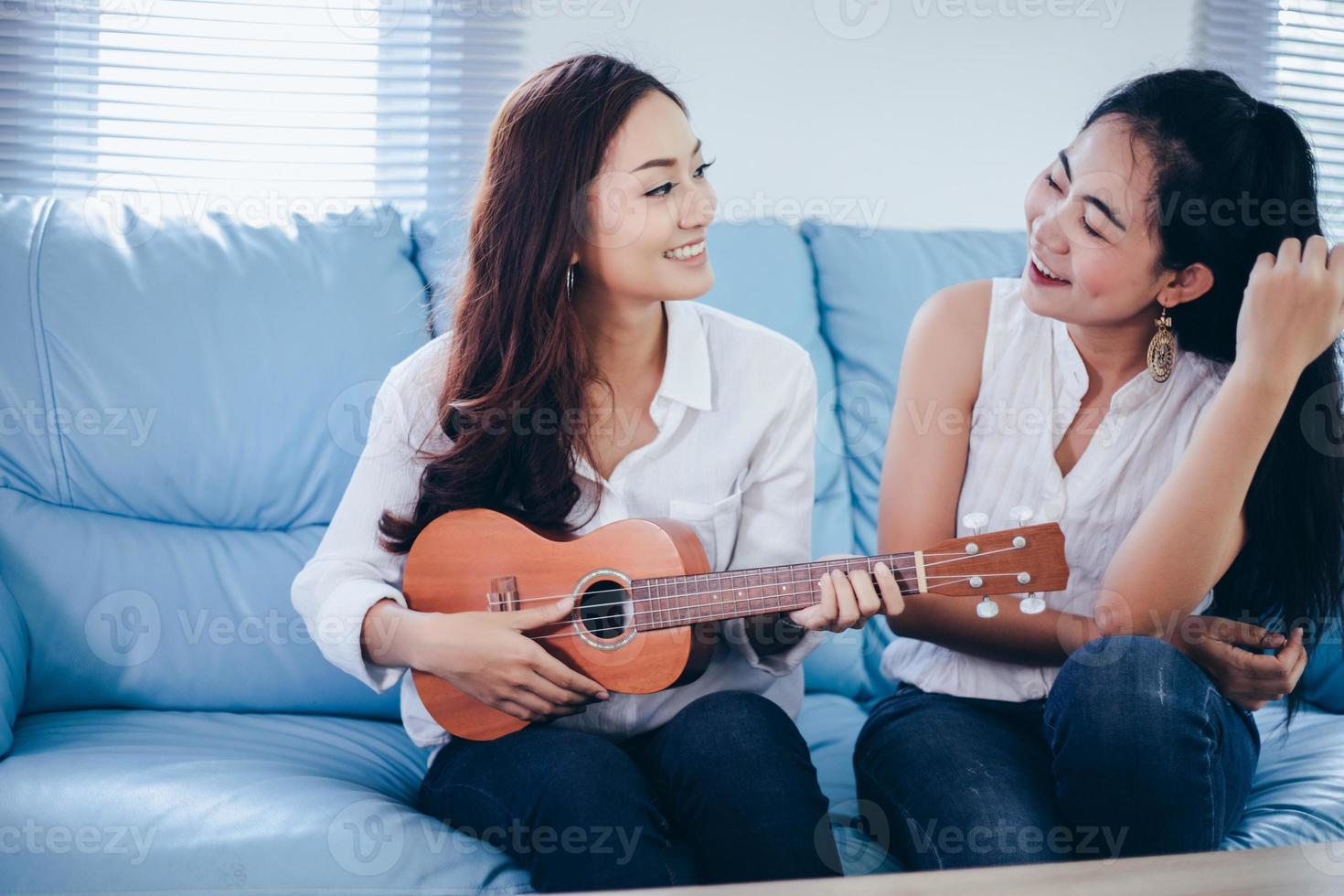 due donne asiatiche si divertono a suonare l'ukulele e sorridono a casa per rilassarsi foto