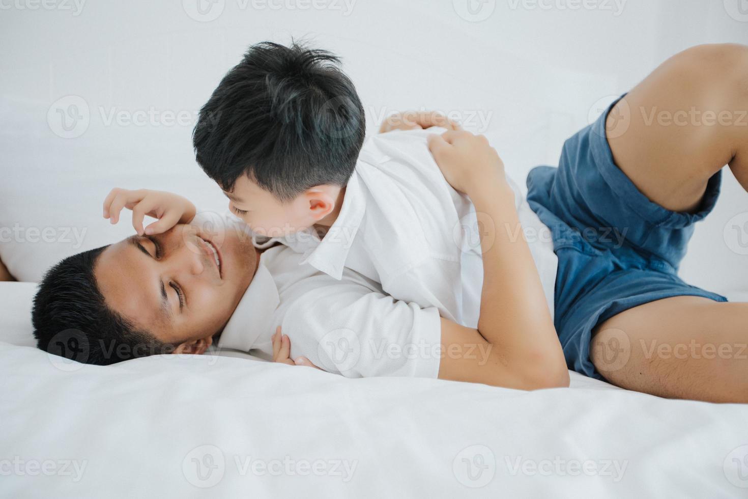 felice famiglia asiatica con figlio a casa in camera da letto che gioca e ride foto