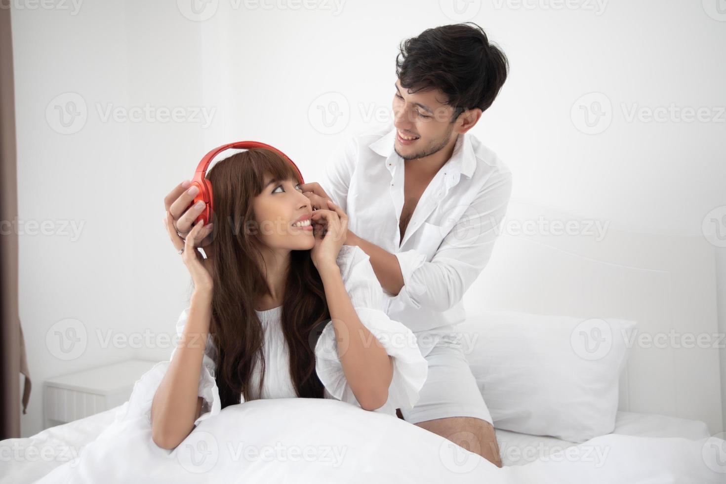 amante delle coppie sdraiato sul letto stile di vita felice e ragazza sorridente che si rilassa e ascolta musica nel letto bianco foto