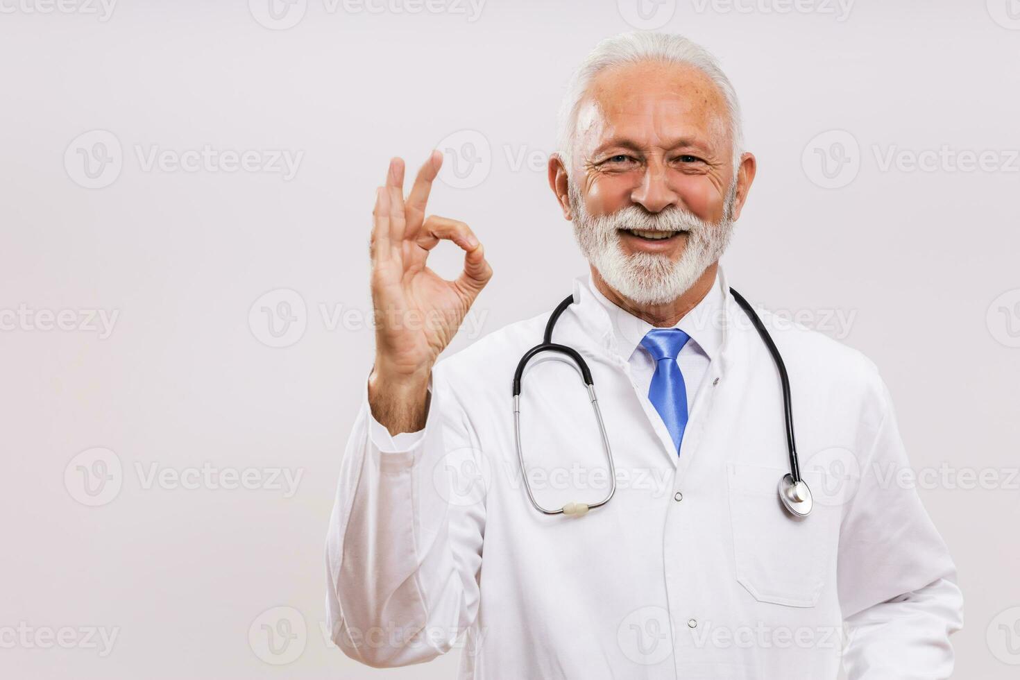 ritratto di anziano medico mostrando ok cartello su grigio sfondo. foto