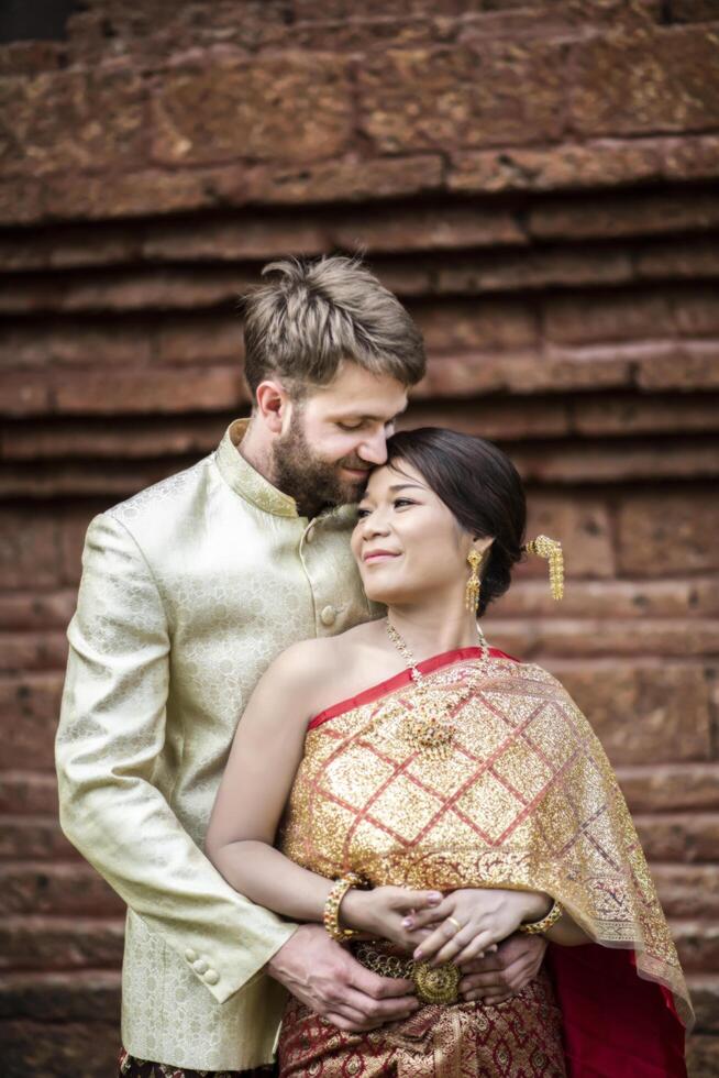 la sposa asiatica e lo sposo caucasico hanno un momento romantico con il vestito thailandese foto