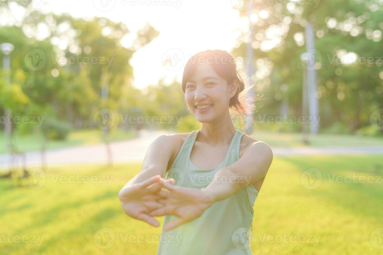 femmina pareggiatore. in forma giovane asiatico donna con verde abbigliamento sportivo allungamento muscolo nel parco prima in esecuzione e godendo un' salutare all'aperto. fitness corridore ragazza nel pubblico parco. benessere essere concetto foto