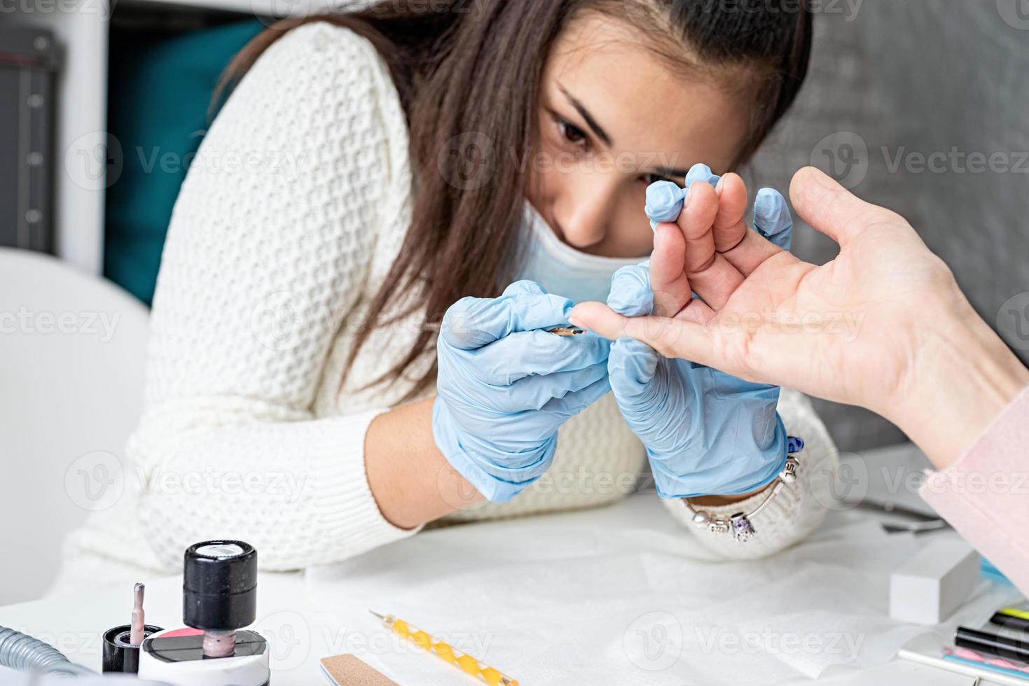 maestro di manicure in maschera e guanti che mettono lo smalto gel sulle unghie di un cliente foto