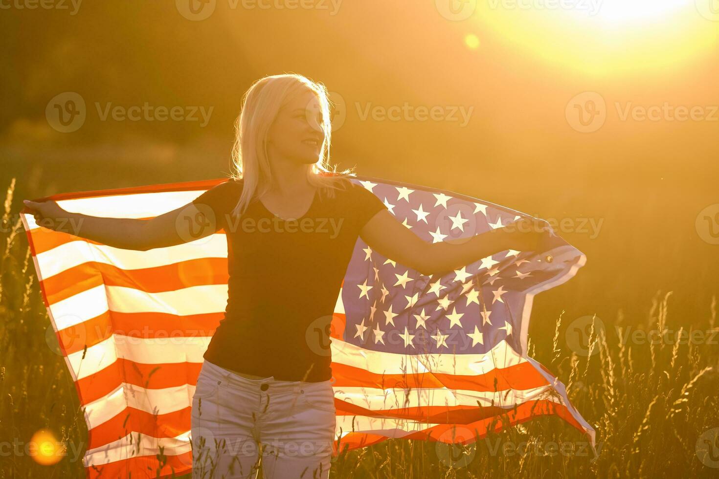 bellissimo giovane ragazza Tenere un americano bandiera nel il vento nel un' campo di segale. estate paesaggio contro il blu cielo. orizzontale orientamento. foto