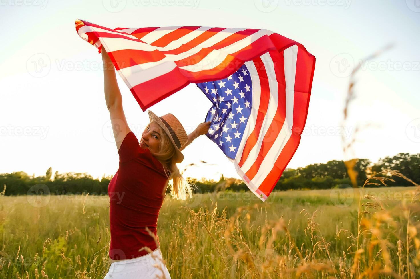bellissimo giovane ragazza Tenere un americano bandiera nel il vento nel un' campo di segale. estate paesaggio contro il blu cielo. orizzontale orientamento. foto
