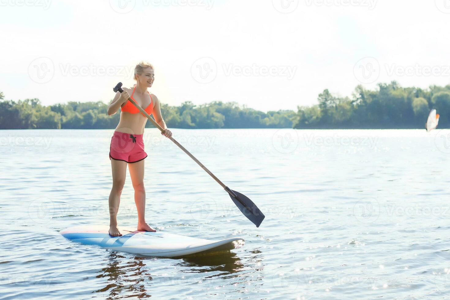 giovane attraente donna su In piedi su pagaia tavola nel il lago, cenare foto