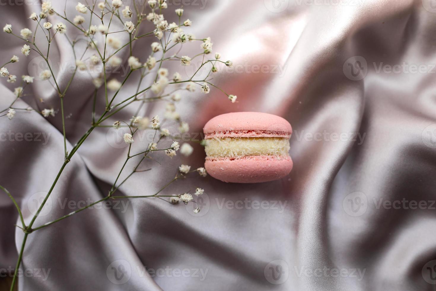 amaretti francesi rosa o biscotti macarons e fiori bianchi su uno sfondo di stoffa. aromi naturali di frutta e bacche, ripieno cremoso per la festa della mamma di San Valentino, Pasqua con cibo d'amore. foto