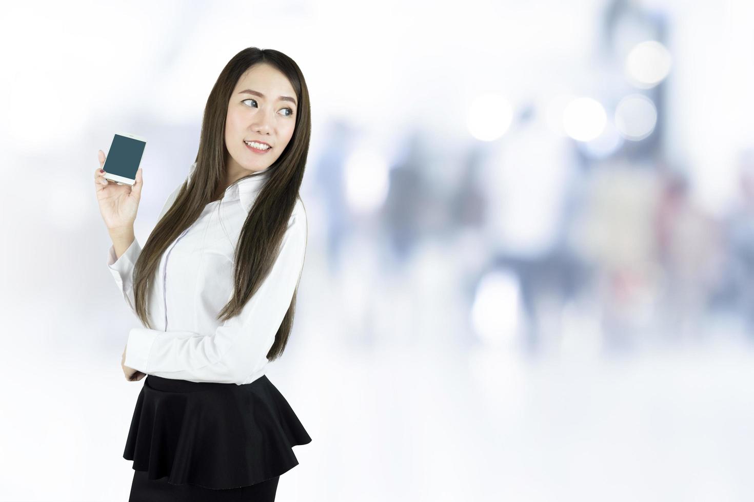 donna d'affari asiatica sorridente, con in mano uno smartphone con schermo vuoto su sfondo sfocato foto