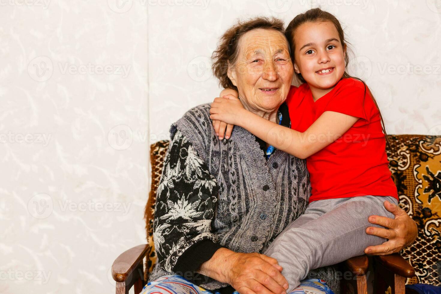 famiglia bonding concetto. bello poco ragazza felicemente abbracciare sua nonna nel leggero vivente camera foto