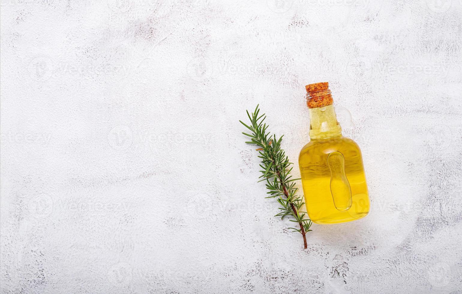 bottiglia di vetro di olio d'oliva e ramo di rosmarino impostato su sfondo di cemento bianco. foto