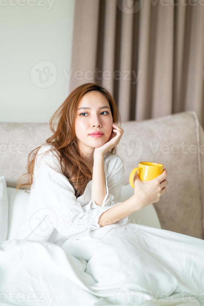 ritratto bella donna sveglia e tenendo tazza di caffè o tazza sul letto foto