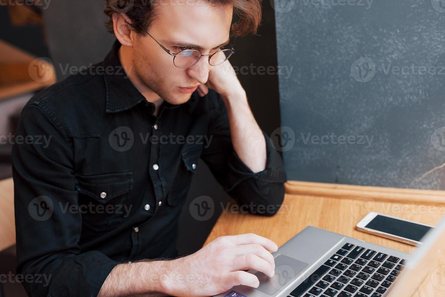 designer uomo creativo che lavora sul suo computer portatile mentre aspetta gli ordini al suo bar preferito al chiuso, studente maschio che lavora su net-book durante la colazione mattutina nell'interno moderno della caffetteria foto