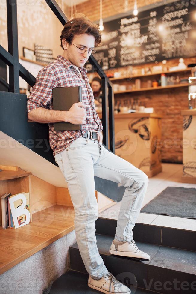 giovane di talento in camicia casual disegno schizzo in taccuino godendo il tempo libero nella caffetteria.studente esperto che scrive i compiti nel blocco note seduto in coworking foto