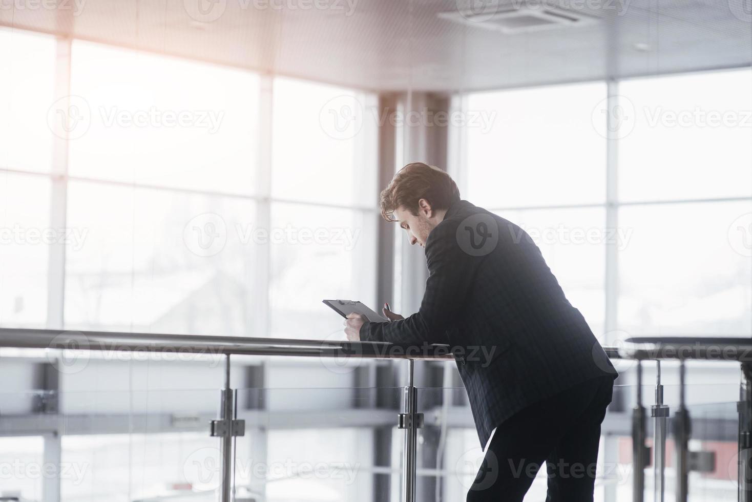 il punto di vista posteriore del giovane leader fiducioso sta riposando dopo un incontro di lavoro con partner stranieri, mentre è in piedi vicino al grande sfondo della finestra dell'ufficio con lo spazio della copia per il tuo messaggio di testo pubblicitario foto