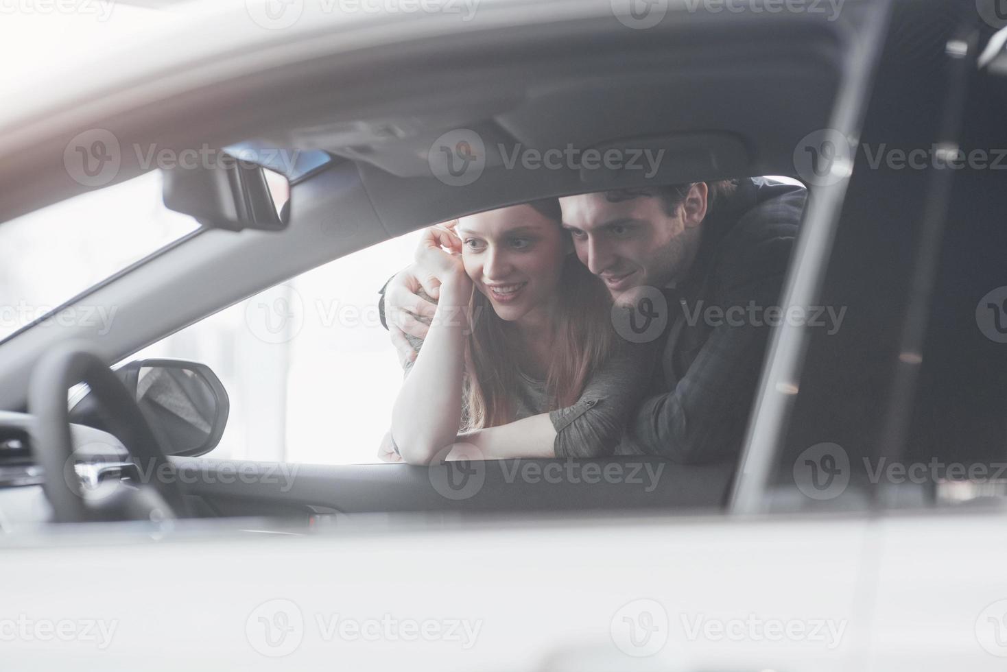 comprando la loro prima auto insieme. vista dall'alto del giovane venditore di auto in piedi presso la concessionaria che racconta le caratteristiche dell'auto ai clienti foto