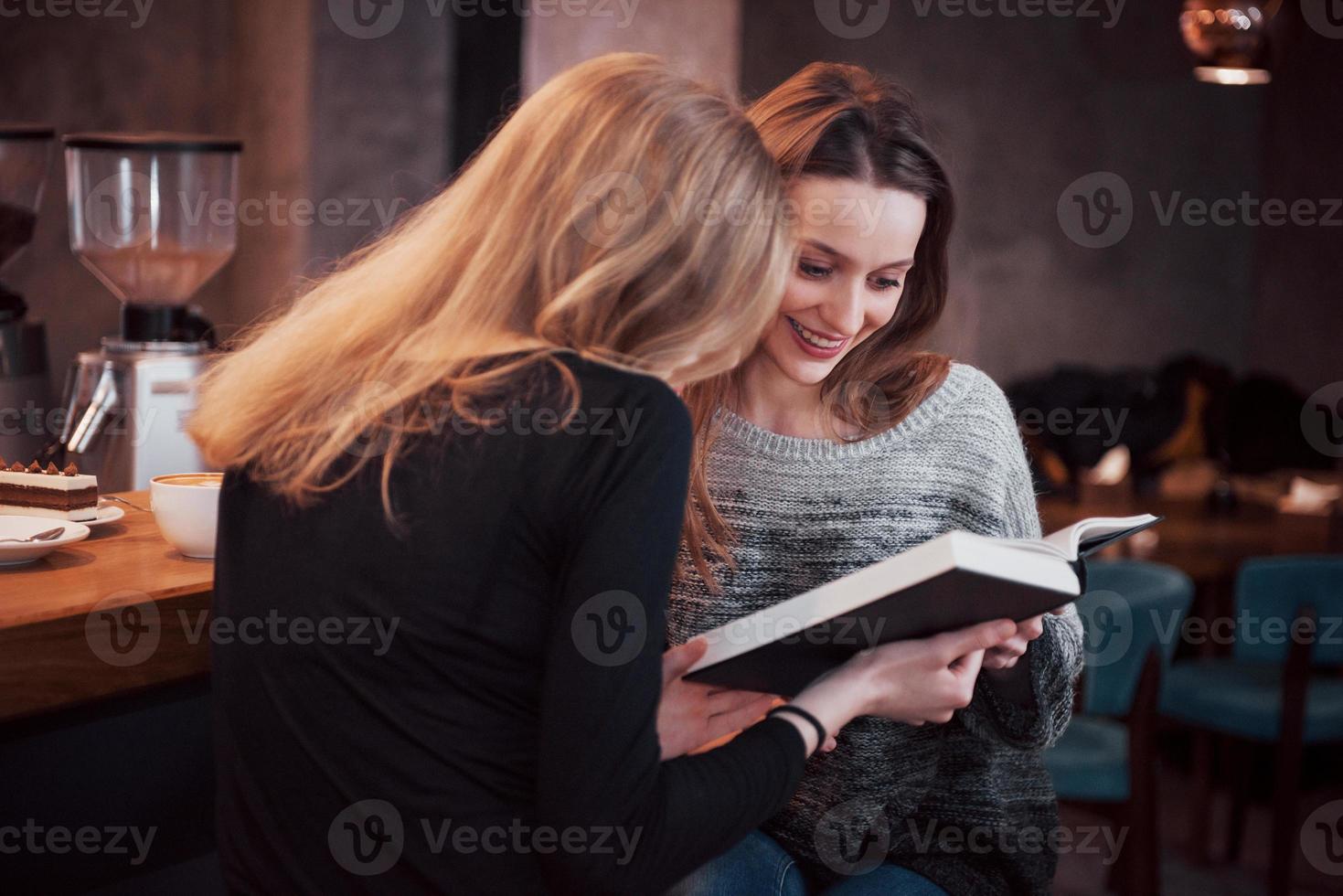 due ragazze assorte nella lettura di un libro durante la pausa al bar. carine e adorabili giovani donne stanno leggendo un libro e bevendo caffè foto