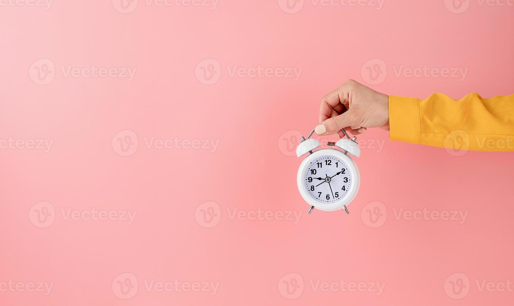 mano femminile che tiene sveglia bianca su sfondo rosa foto