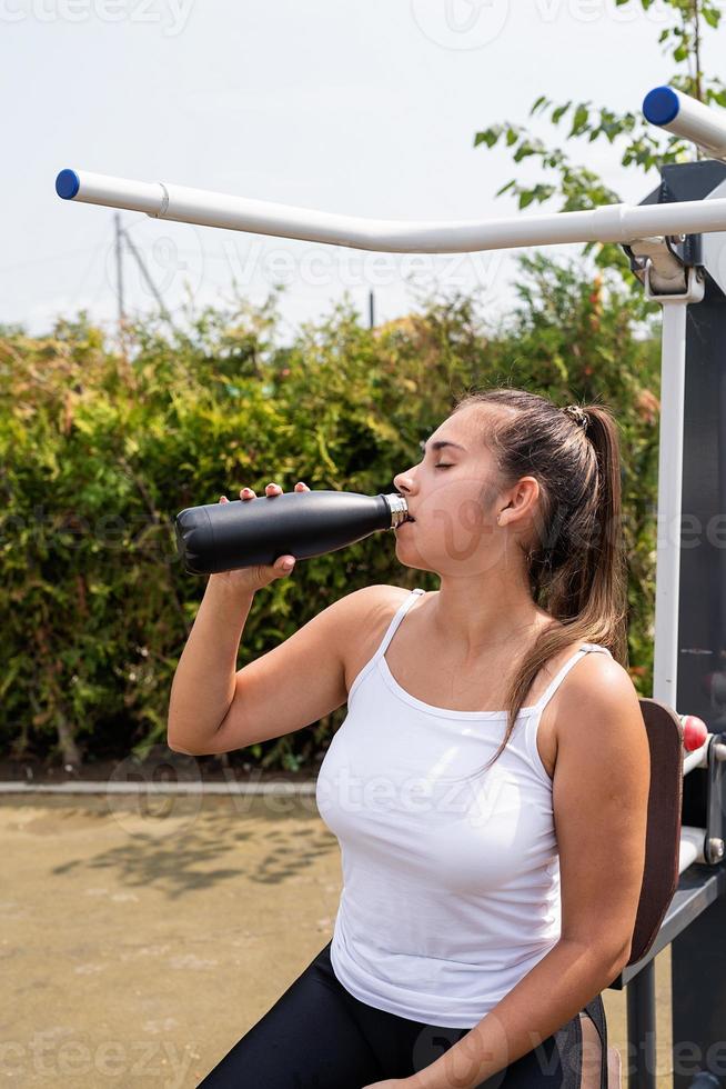 donna felice che si allena sul campo sportivo nella soleggiata giornata estiva, bevendo acqua dalla bottiglia foto