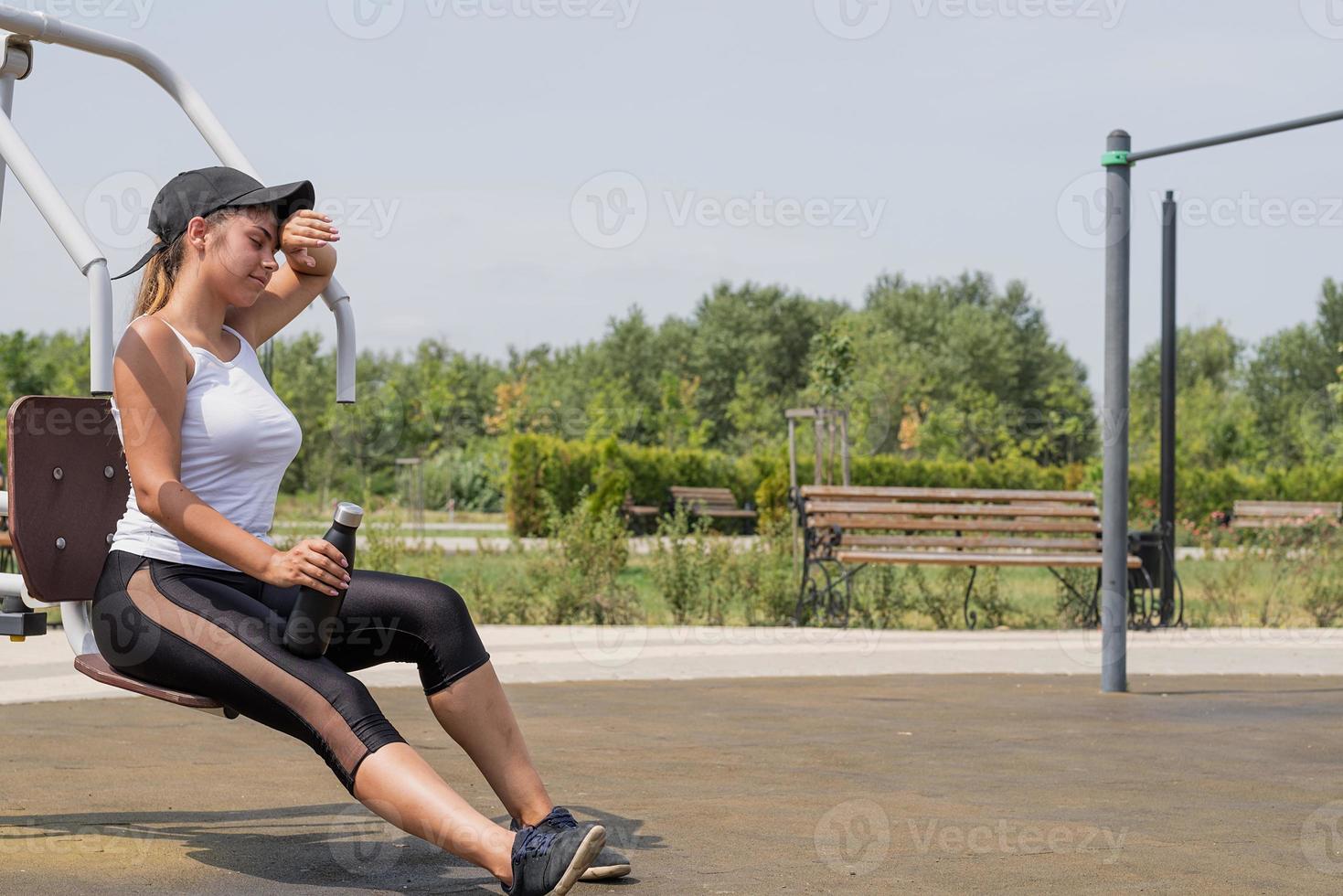 donna felice che si allena sul campo sportivo nella soleggiata giornata estiva, bevendo acqua dalla bottiglia, riposandosi foto