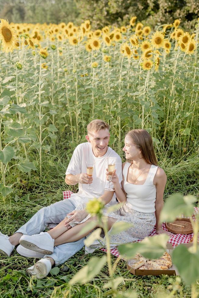 giovane coppia che fa picnic sul campo di girasoli al tramonto foto