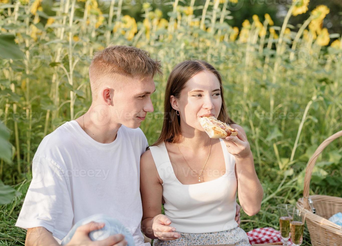 giovane coppia che fa picnic sul campo di girasoli al tramonto foto