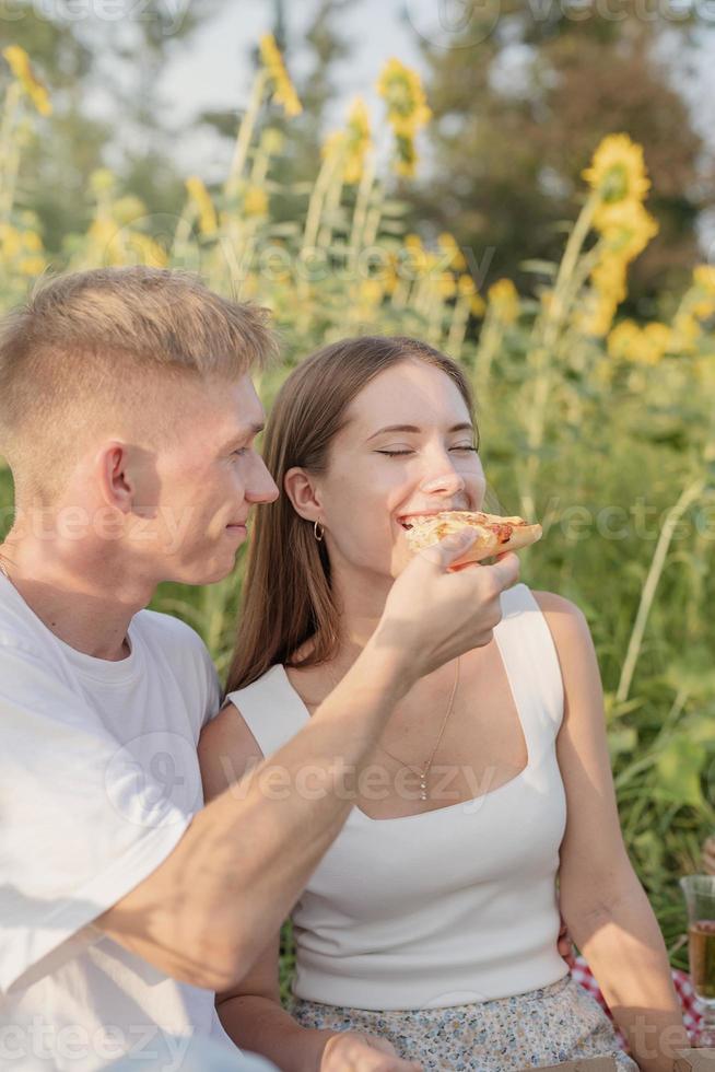 giovane coppia che fa picnic sul campo di girasoli al tramonto foto