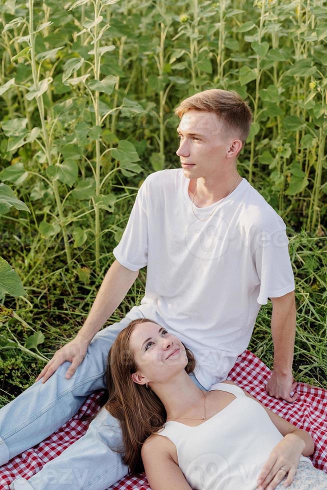 giovane coppia che fa picnic sul campo di girasoli al tramonto foto