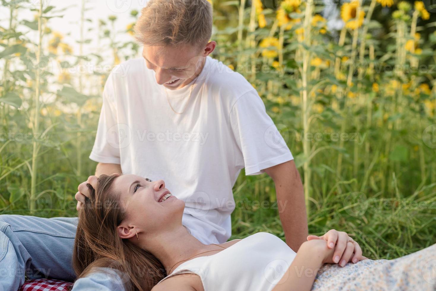 giovane coppia che fa picnic sul campo di girasoli al tramonto foto