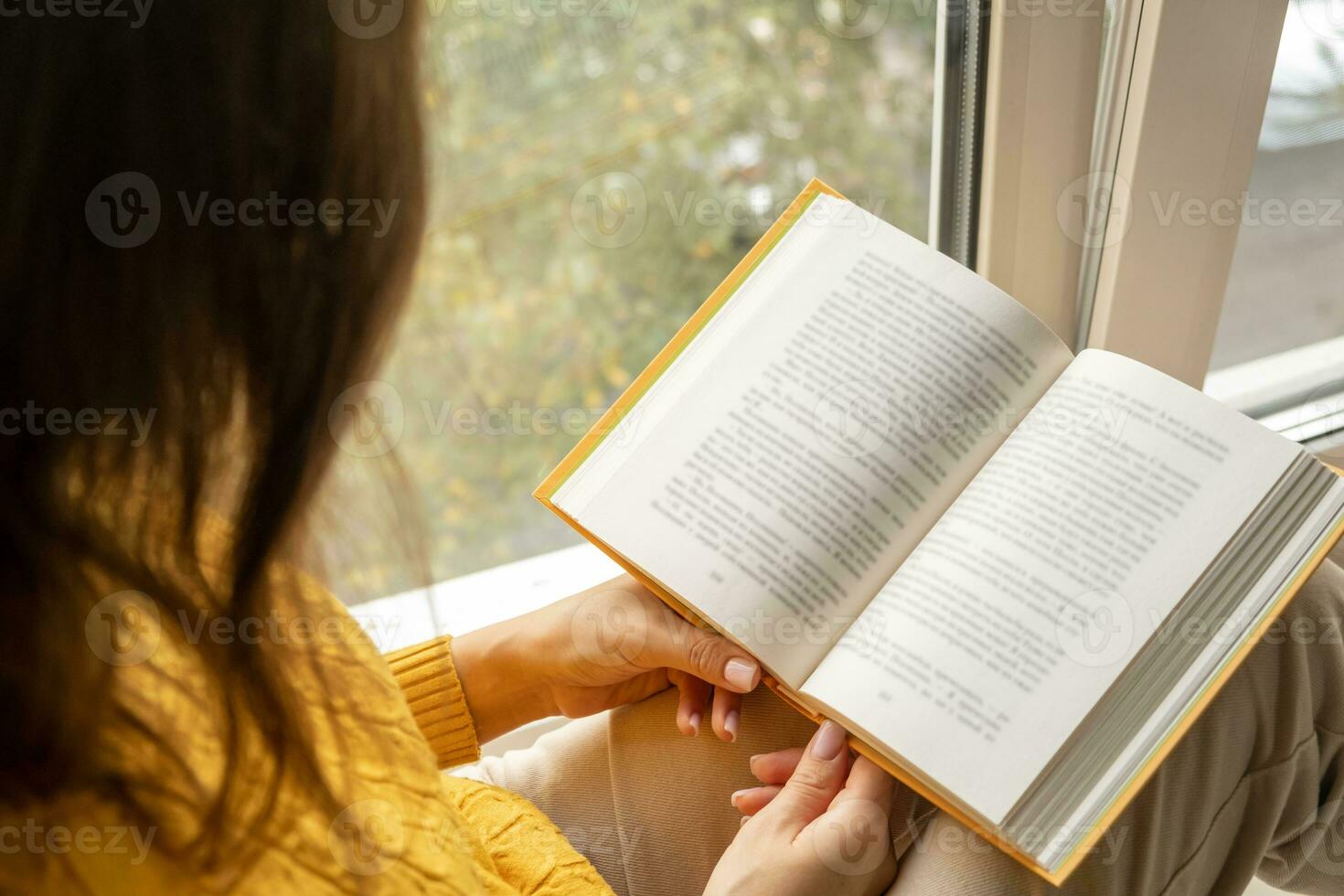 giovane bellissimo donna vicino finestra giallo a maglia maglione leggere libro foto