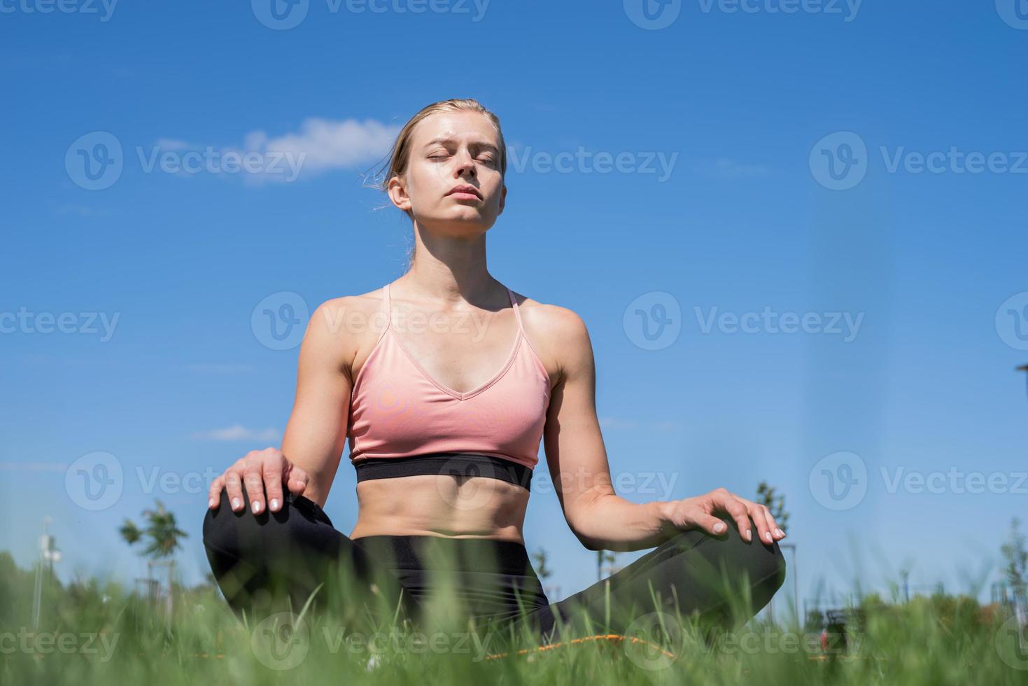 donna sportiva che medita seduta sull'erba sotto il cielo blu foto