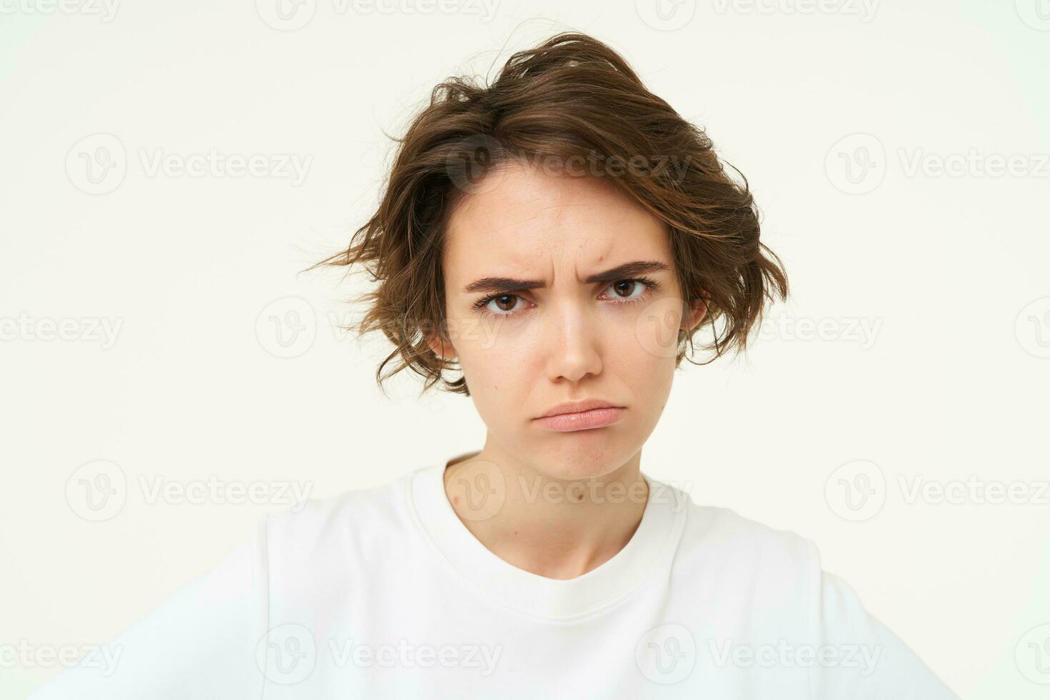 ritratto di accigliato, scontroso giovane donna, sembra irritato e offeso, deluso di qualche cosa, in piedi al di sopra di bianca sfondo foto