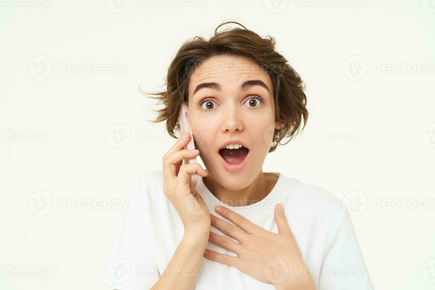 ritratto di donna con sorpreso viso, risposte Telefono chiamata e sembra emozionato, stupito di grande notizia, sta al di sopra di bianca sfondo foto