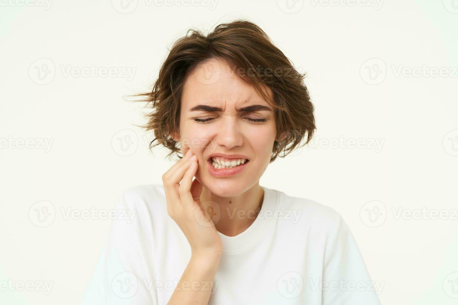 vicino su di brunetta donna tocchi sua dente, ha un' mal di denti, dentale problema, doloroso disagio nel bocca, sta al di sopra di bianca sfondo foto