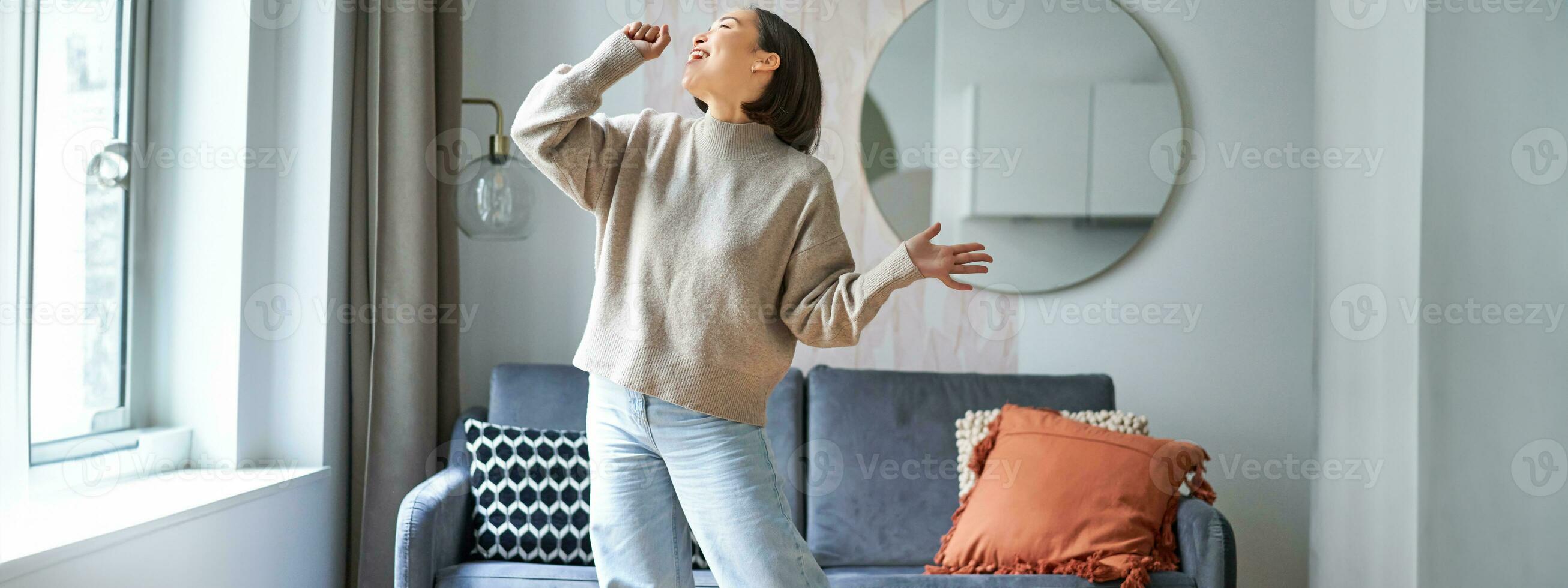 persone e emozioni. ritratto di asiatico ragazza in piedi nel vivente camera, cantando nel ombra microfono, danza e avendo divertimento, sensazione gioia foto